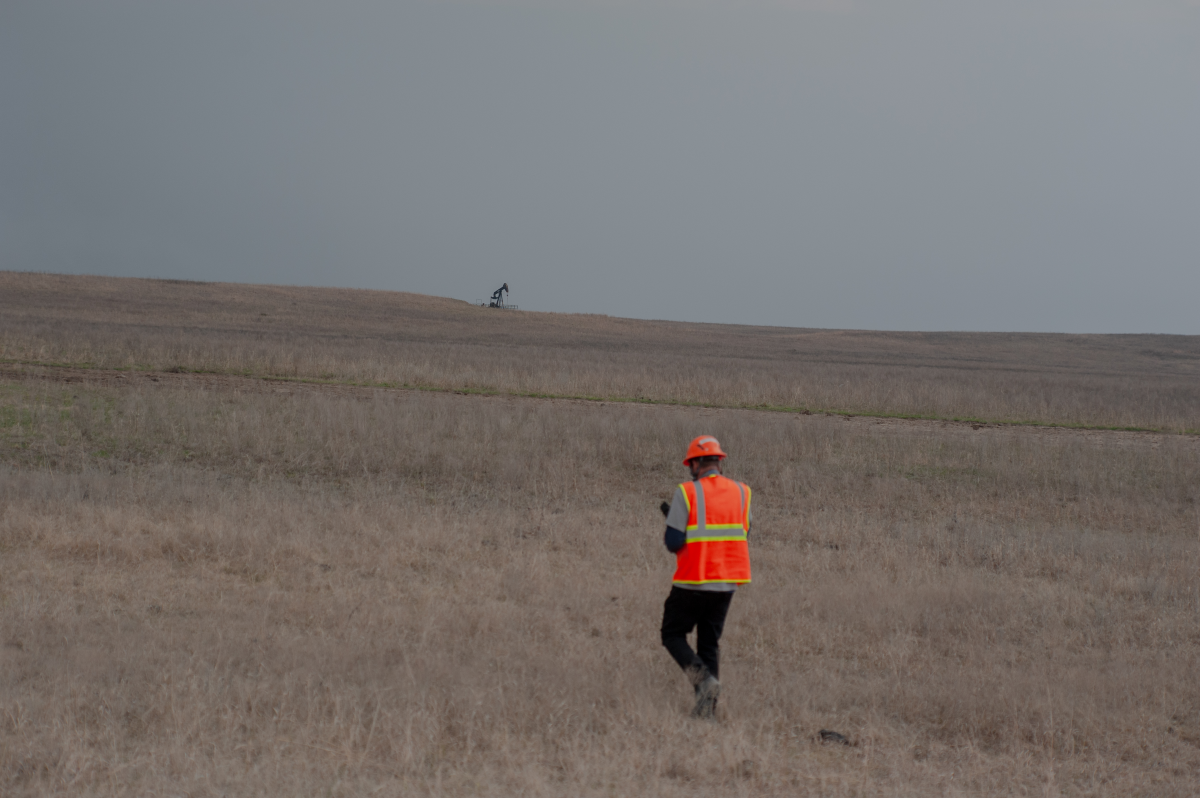Caldwell walks through dry grass in the Tallgrass Prairie Preserve in Oklahoma on March 20, 2024. A pumpjack is visible in the distance.