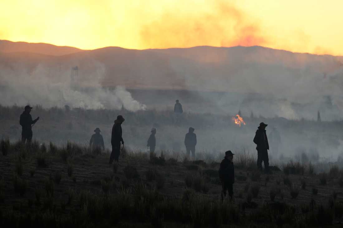 Anti-government protesters standing in a field are silhouetted against clouds of tear gas launched by police, near El Alto, Bolivia, Saturday, May 16, 2026.