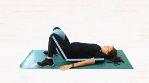 A woman lying on a mat with her knees raised up as a blue ball is positioned in between them.