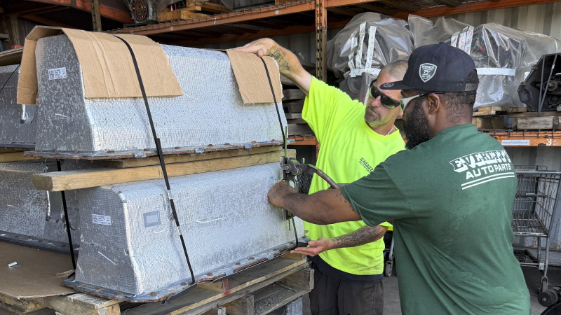 Chris McQuiggen and Archie Brewton of Everett Auto Parts strap two Chevy Volt batteries to a pallet in preparation for shipping. The batteries are separated by a layer of wood so they don't make contact with each other. Everett Auto Parts found a battery recycler who will accept these hybrid vehicle batteries, but the salvage yard won't make any money off of them.