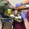 The mid-range photograph focuses on the arm and hands of medical assistant Izzy Kadrmas and patient Tywon Pugh.