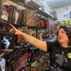 A woman points at a box containing an Annabelle doll displayed on the pegboard wall of a toy store. 