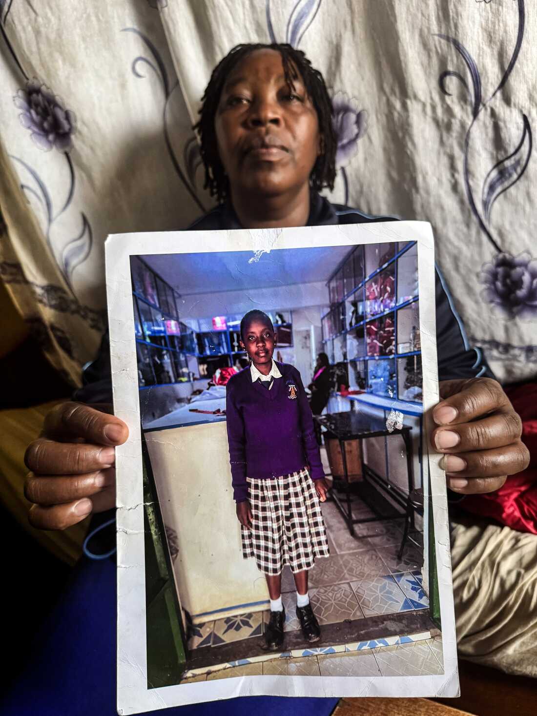 Rachael Wanjiru, a 43-year-old woman, holds a photo of her 16-year-old daughter, Purity Wamboi. In the photo, Purity is wearing a navy blue sweater and a black-and-white plaid skirt.