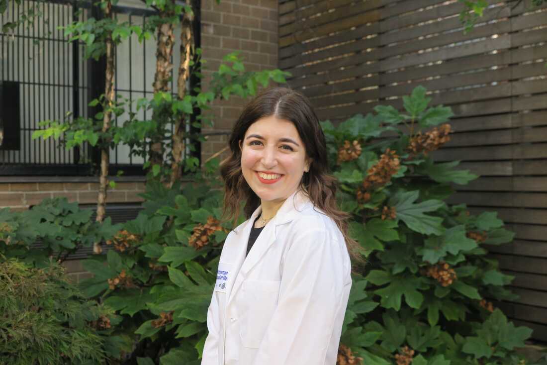 EJ Beck is shown in her white medical coat. She has a bright smile on her face.