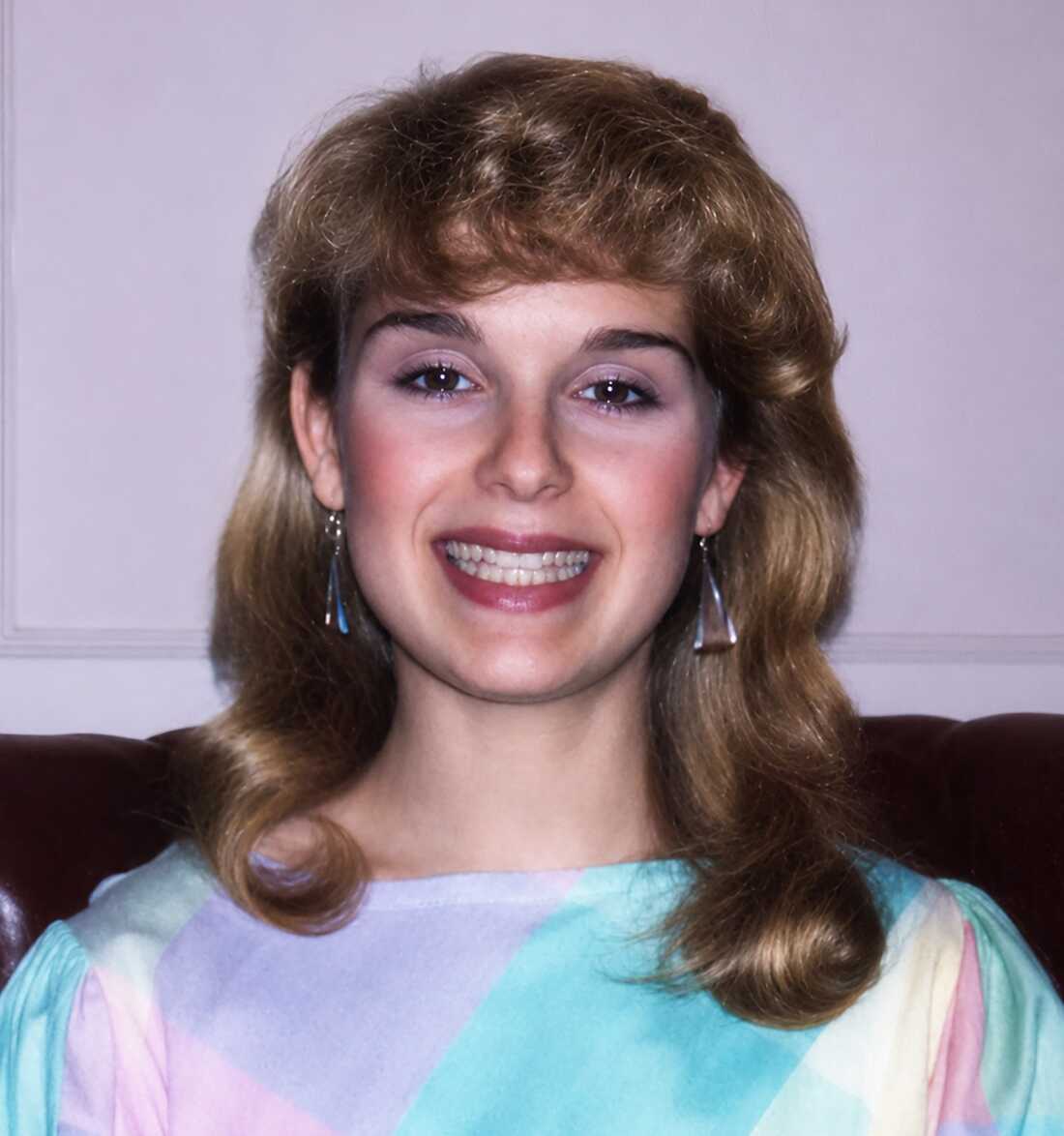This photo shows Solitaire Miles photographed from about the shoulders up. The young woman is wearing pastel colors and dangling earrings. Her hair is styled with bangs, and she's smiling.