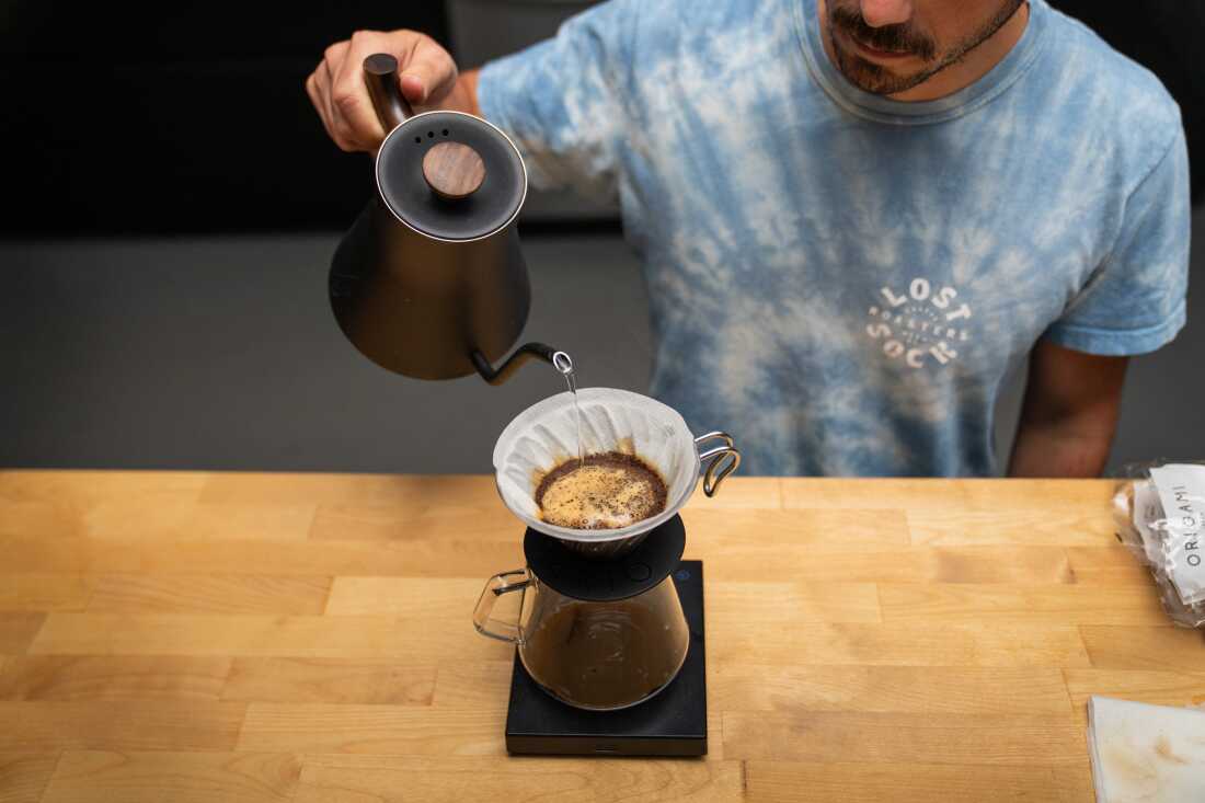 In this photo, Jeff Yerxa is pouring hot water from a kettle with a spout into a coffeepot with a filter and coffee on top of it.