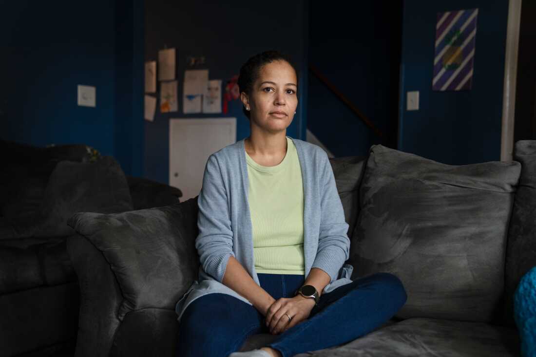 Stephani Cherkaoui sits cross-legged on a gray sofa. She's wearing blue jeans, a light-colored shirt and a light blue cardigan.