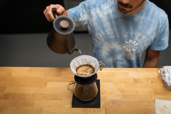 In this photo, Jeff Yerxa is pouring hot water from a kettle with a spout into a coffeepot with a filter and coffee on top of it.
