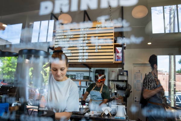 Kristen Tizaawie-Vogel prepares a drink at Lost Sock Roasters' coffee shop in the Takoma neighborhood of Washington, D.C. Behind her are two workers and a menu board displaying prices.