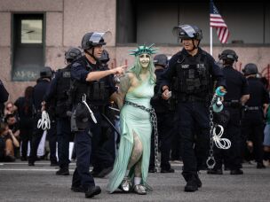 LAPD officers arrest a protester dressed as Lady Liberty in chains following clashes near the Metropolitan Detention Center during the
