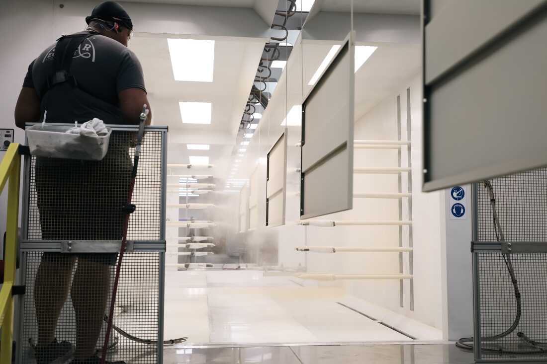 A Virco employee watches as automated paint guns spray powder onto furniture components moving through the electrostatic powder coat booth.