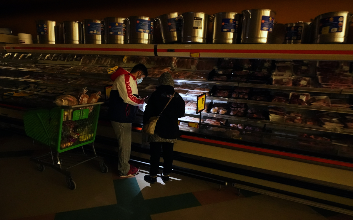 In this Tuesday, Feb. 16, 2021 photo, customers use the light from a cell phone to look in the meat section of a grocery store that was without power, in Dallas.