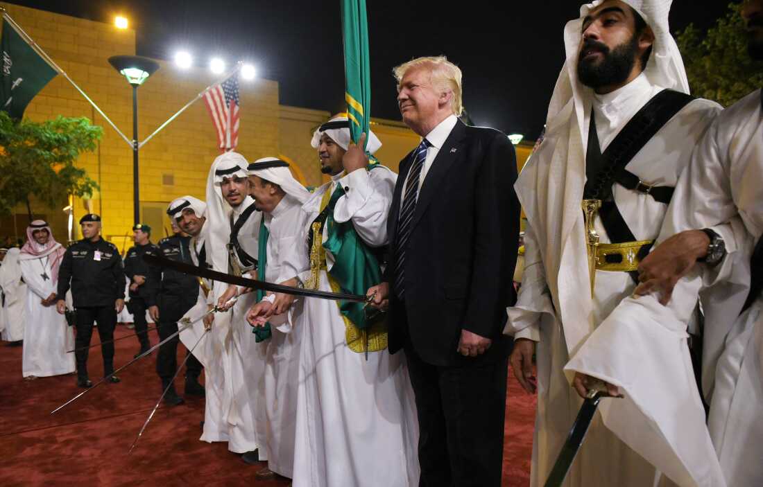 In this 2017 photo, taken at a welcome ceremony in Riyadh, Saudi Arabia, President Trump is wearing a dark suit and holding a sword while flanked by men wearing traditional white robes who are also holding swords.