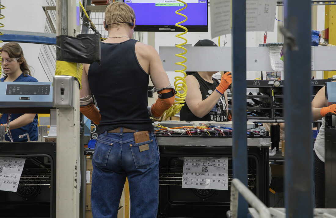 At least five people work on an assembly line handling electronic components.