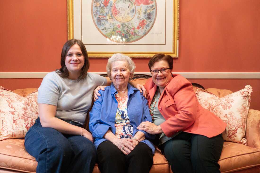 Caroline, Barbara and Cynthia sit together on a pink couch with a terracotta colored wall behind them.