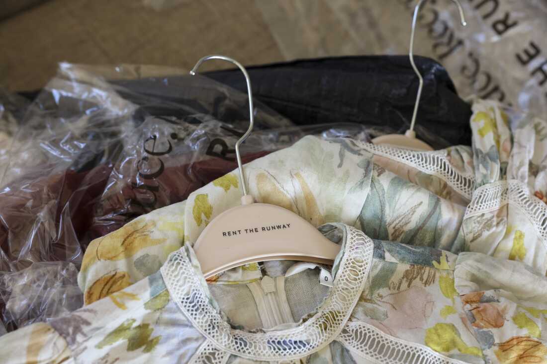 A floral dress on a Rent the Runway hanger rests on top of other outfits wrapped in plastic.