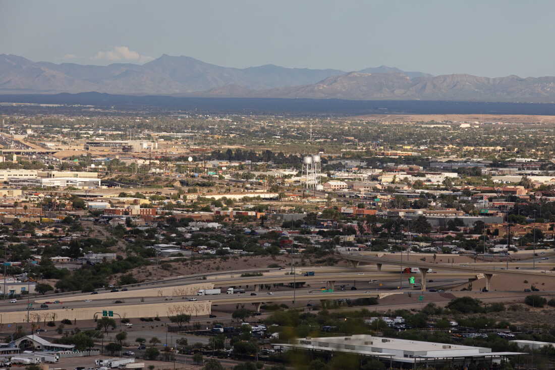 This photo shows a vista view of Tucson, Arizona, with its buildings and highways. Mountains rise up in the background.