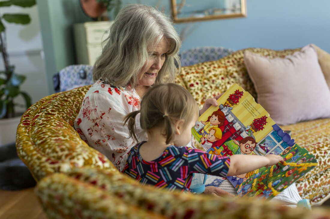 Mary Jo Galusha reads a book to her granddaughter, Robin, 23 months, at her home in Newark, Delaware. The two are sitting on a sofa together.