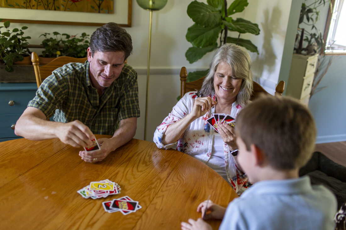 Mary Jo Galusha; her grandson, George; and her son-in-law, Michael Blacketer, sit around a wooden table while they play the card game Uno at her home in Newark, Delaware.