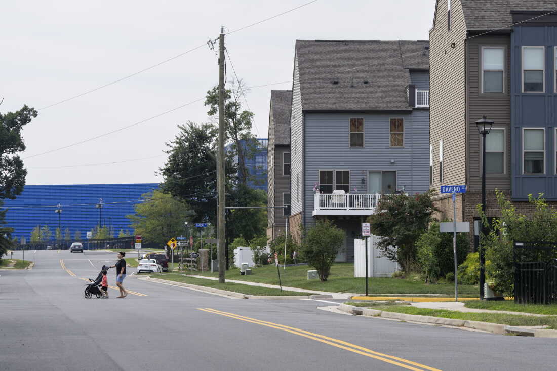 The Vantage VA2 data center, in a long blue building, sits in the background, with multistory residential buildings in the foreground, in Sterling, Virginia.