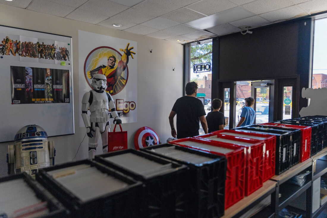 A man and two boys walk by lifesize models of R2-D2 and a Stormtrooper from Star Wars as they exit the store.