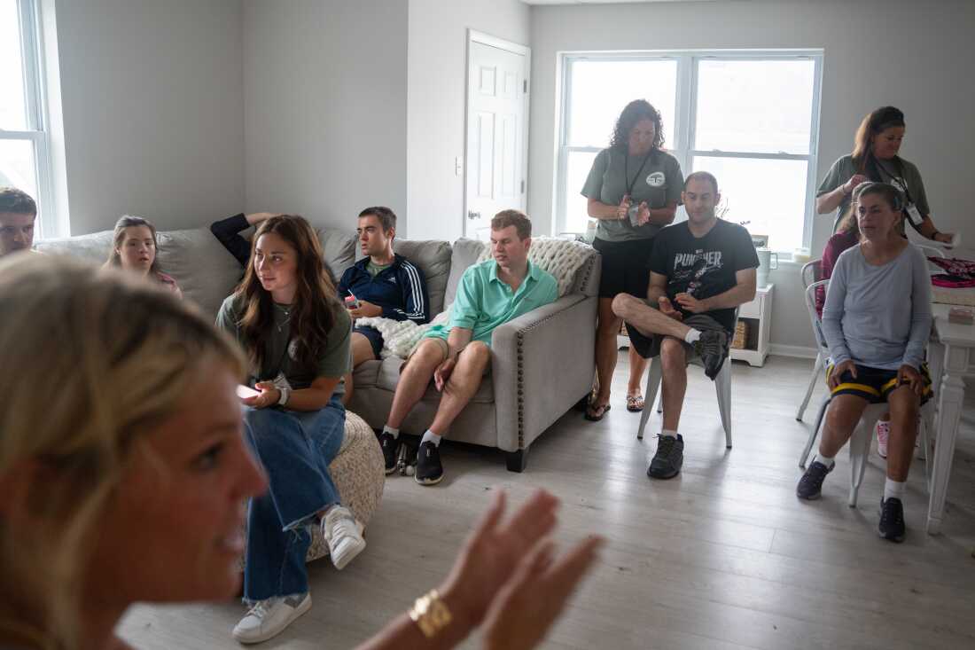 At Next Steps, Cody attends the morning meeting where he and other participants share what they did over the weekend. The participants are sitting on a sofa and chairs in a room.