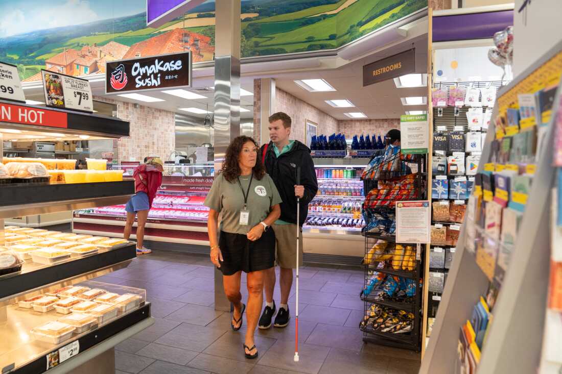 Cody Brendle, holding a white cane, walks in a grocery store with Christine Gaven from the Next Steps program.