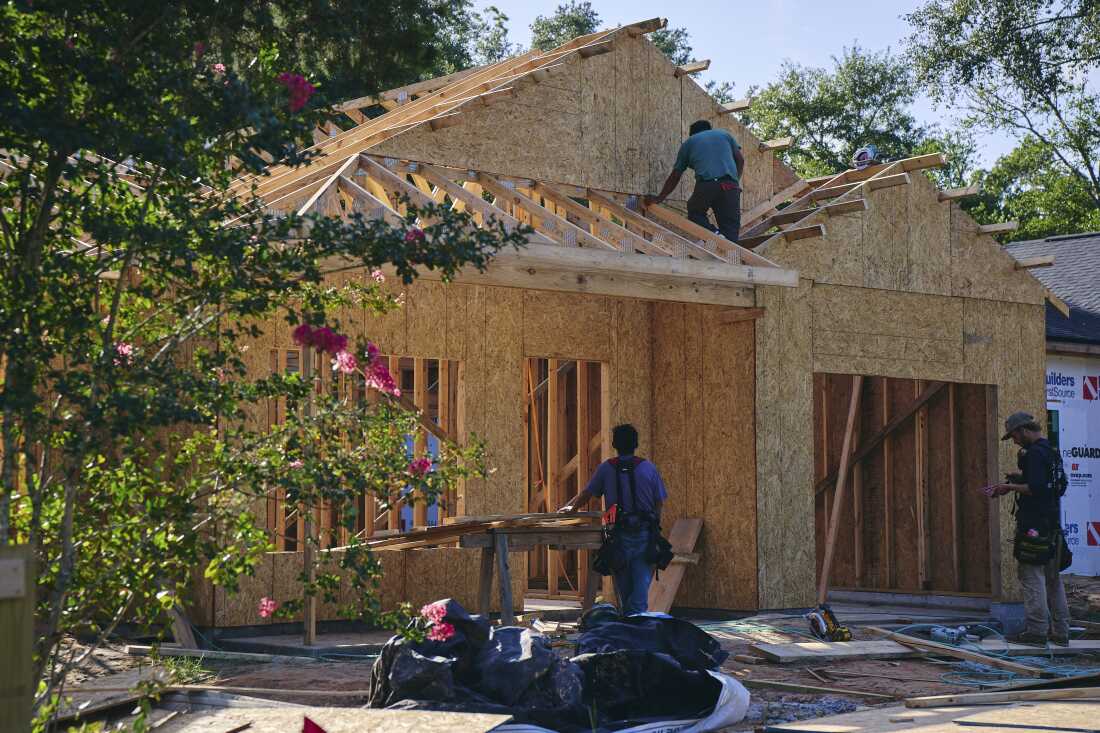 Three men work on a structure under construction in Walton County. The unfinished structure has a skeleton of lumber and plywood.