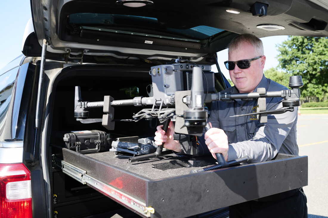 Kevin Fennessy, Chief Warrant Officer, lifts an Ocean County Sheriff's Office DJI M300T drone out of the custom-built bed of a department SUV at Robert J. Miller Airpark, the temporary home of the department, September 4, 2026. These larger drones can be used with a thermal-capable camera payload for search and rescue or with a dropper payload to aid in water rescue. Albert Yee for NPR.