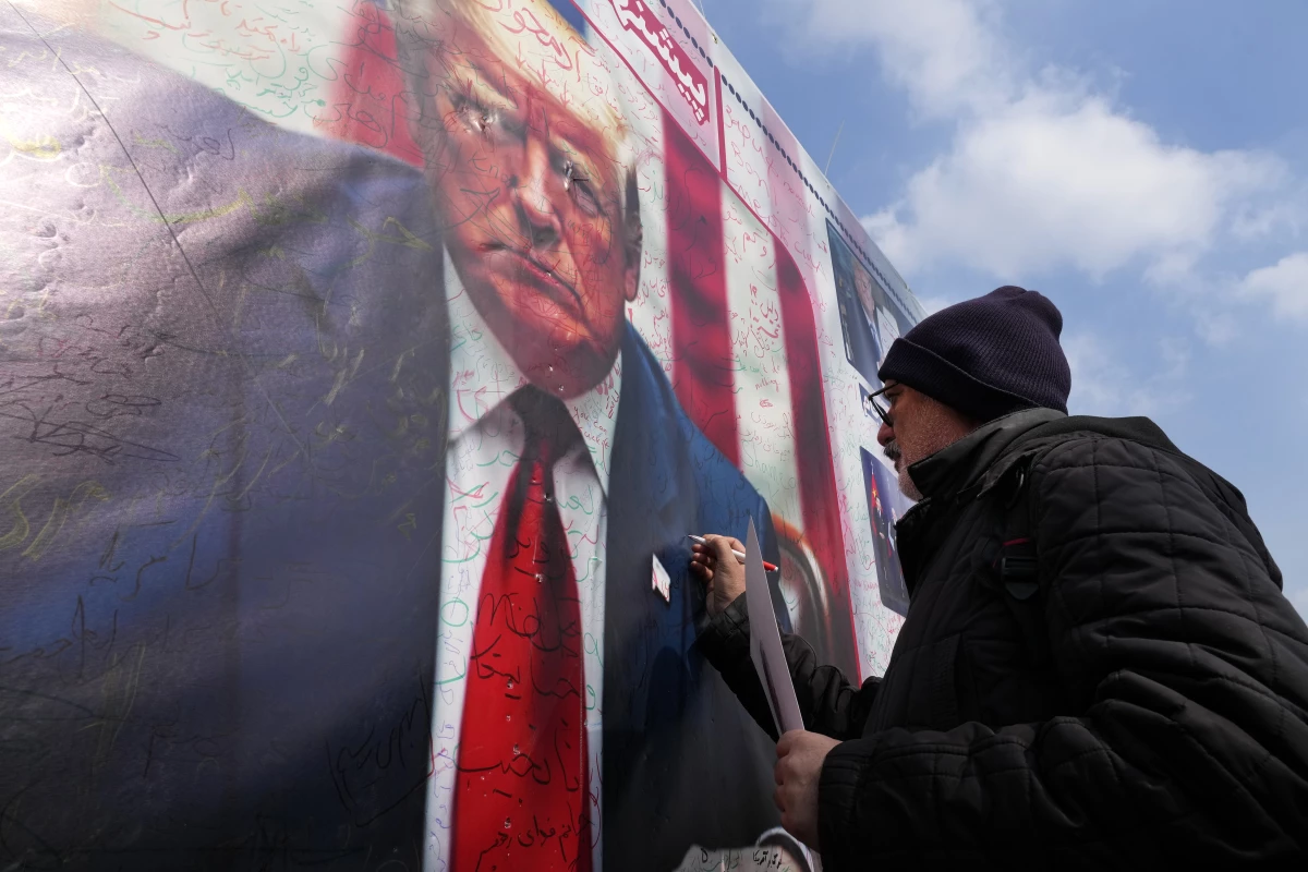 A man writes a slogan on a portrait of the U.S. President Donald Trump during a rally commemorating anniversary of Iran's 1979 Islamic Revolution that toppled the late pro-U.S. Shah Mohammad Reza Pahlavi and brought Islamic clerics to power, in Tehran, Iran, Monday, Feb. 10, 2025. Trump says the US and Iran will have direct nuclear talks soon.