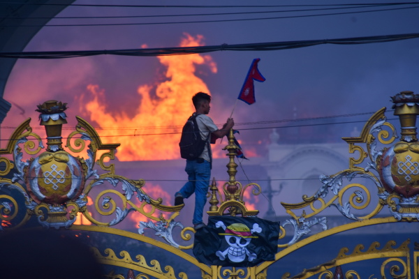 A man hanging a pirate flag as smoke and flames rise from the Singha Durbar, the seat of Nepal government's various ministers offices in Kathmandu, Sept. 9, 2025.