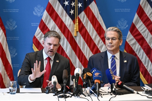 In this photo, Treasury Secretary Scott Bessent and U.S. trade representative Jamieson Greer sit at a table with many microphones on it as they hold a news conference in Geneva on May 12. Both men are wearing suits, and Bessent is on the right side of the frame, while Greer is on the left. American flags are displayed in the background.