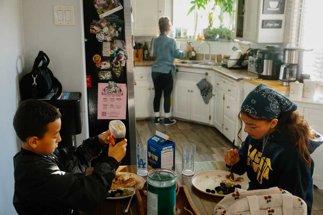 Serrato cleans up the kitchen while her children, J.J. and Laylah, eat breakfast before school.