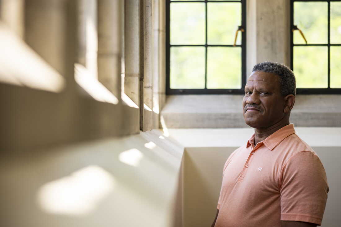 Alvin Tillery stands outside his office at Northwestern University's campus in Evanston, Illinois. He's facing a row of windows, with his head turned toward the camera. He's wearing a peach polo shirt.