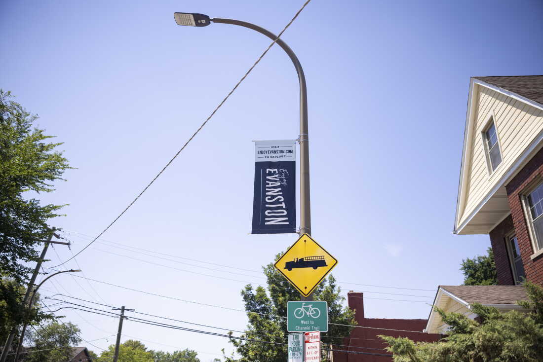 A vertical navy-blue banner with the words "Enjoy Evanston" in white is displayed on the pole of a streetlight outside the office of the nonprofit FirstRepair in Evanston, Illinois, on July 13, 2026.