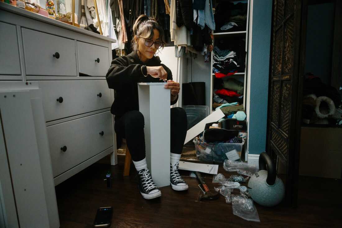 Serrato assembles a piece of furniture at home while she talks to her partner on the phone.
