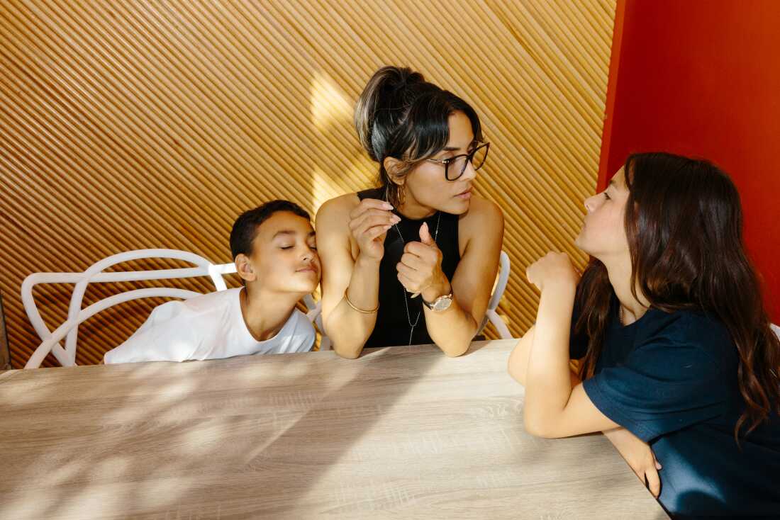 They are all seated at a table as J.J. leans against his mom's arm while she talks with her daughter, Layla.