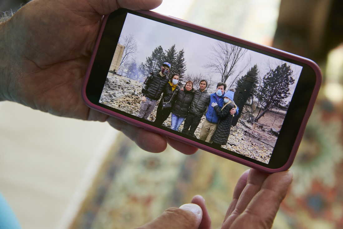 Louie Delaware holds his phone showing a photo of his family outside of their burned home after the Marshall Fire, which destroyed more than 1,100 homes in Louisville, Superior and unincorporated Boulder County. Wildfires are among the climate-related impacts at the center of Boulder County’s lawsuit against ExxonMobil and Suncor Energy. (Jimena Peck for NPR)