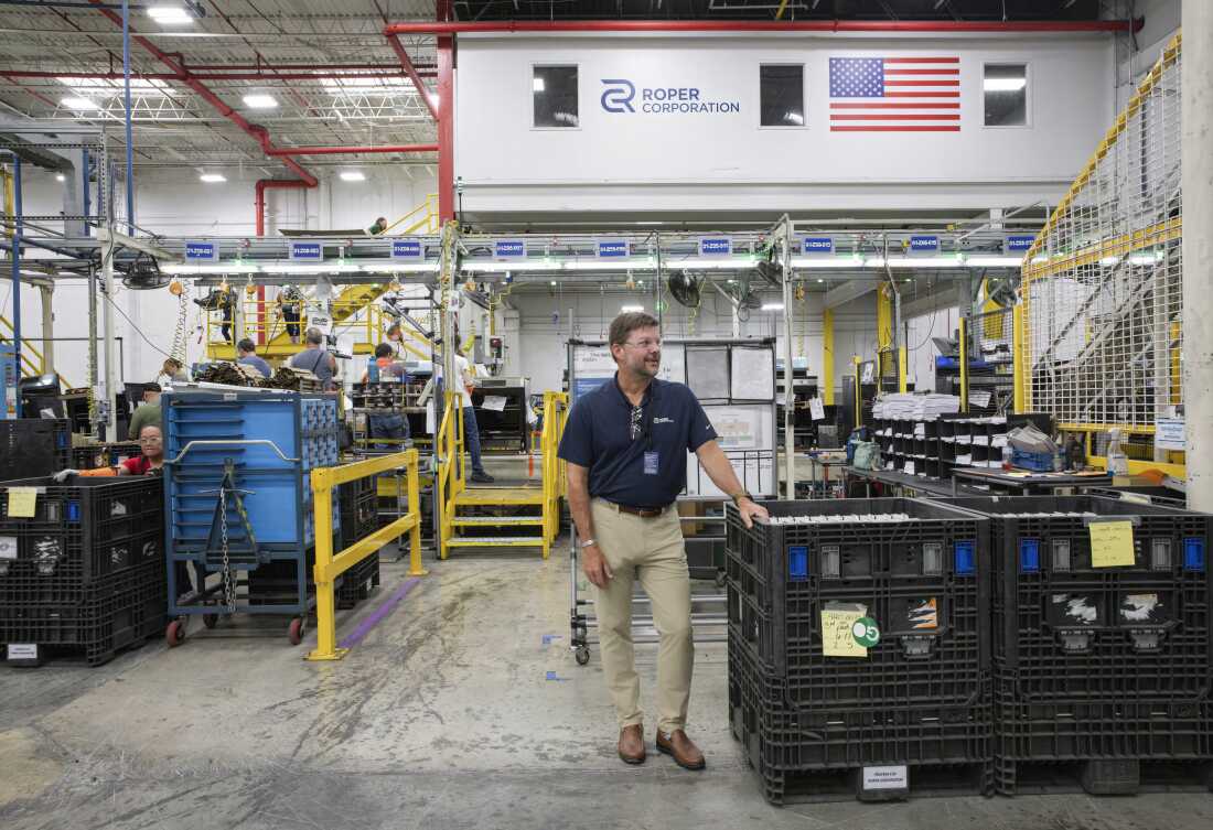 Tony Gabbert is standing on the factory floor, wearing safety glasses, a navy polo shirt and khaki pants. Workers are going about their jobs behind him.