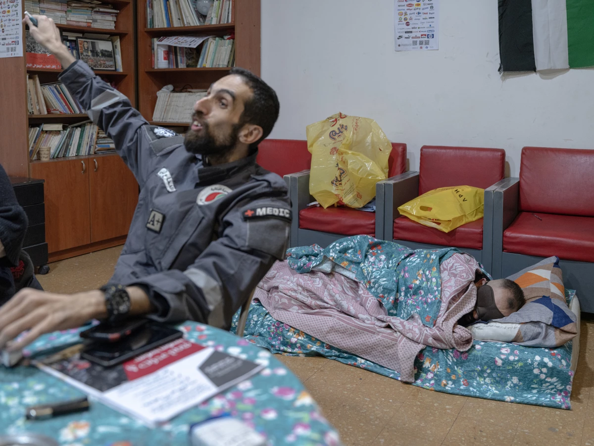 A volunteer gestures at colleagues while another volunteer sleeps behind him. Many sleep at the emergency center, where they are on call day and night. They have had to flee their homes in areas where Israel carried out its heaviest bombardments.