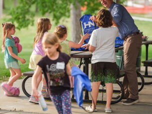 Chris Sommerich, Executive Director of Humanities Nebraska, hands out bags to students during Prime Time Family Reading at Henry Park in Lincoln, Neb. on May 14, 2026. The program was led by a storyteller and discussion leader for underserved children and their families to read and discuss award-winning children's books.