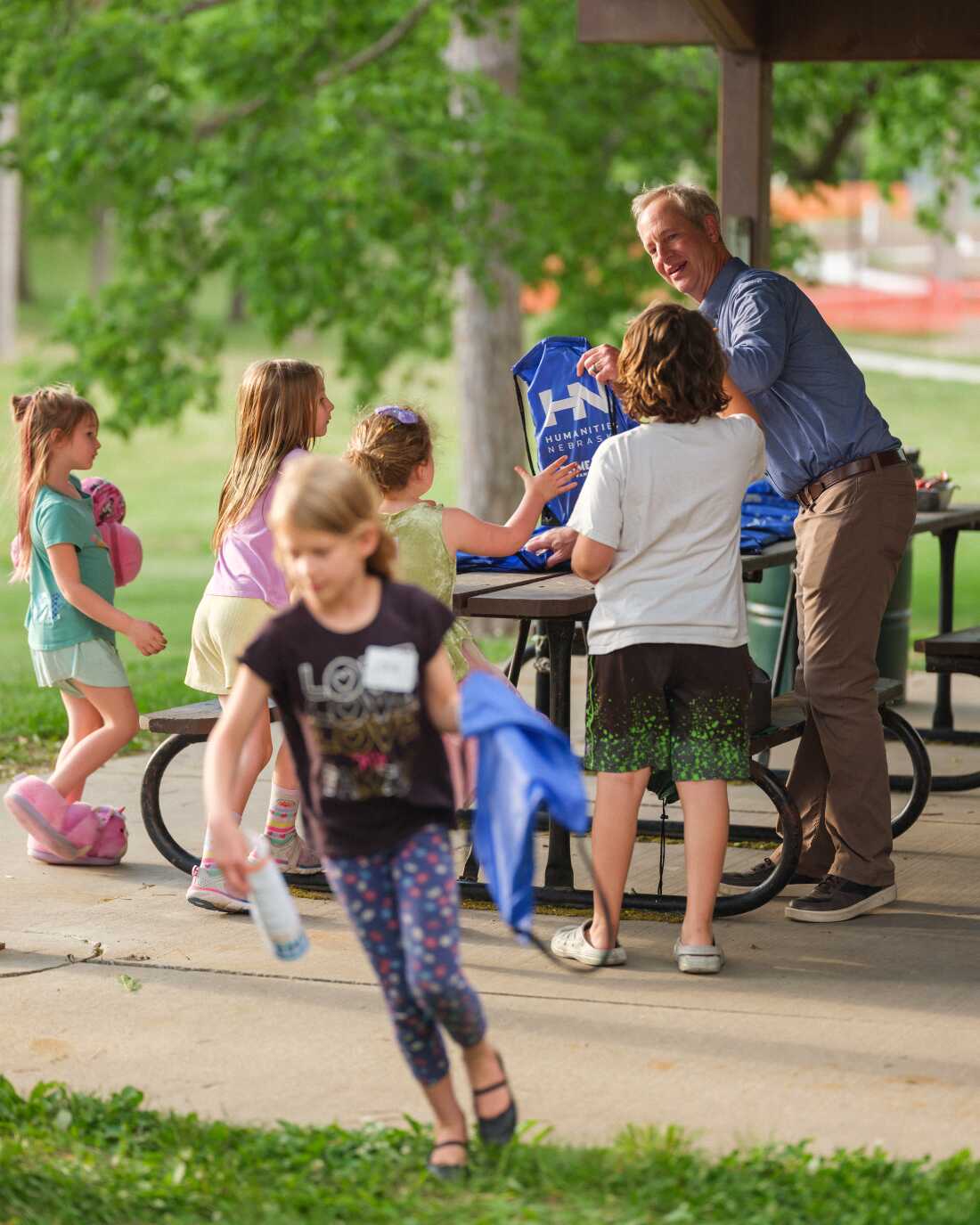 Chris Sommerich, Executive Director of Humanities Nebraska, hands out bags to students during Prime Time Family Reading at Henry Park in Lincoln, Neb. on May 14, 2026. The program was led by a storyteller and discussion leader for underserved children and their families to read and discuss award-winning children’s books.