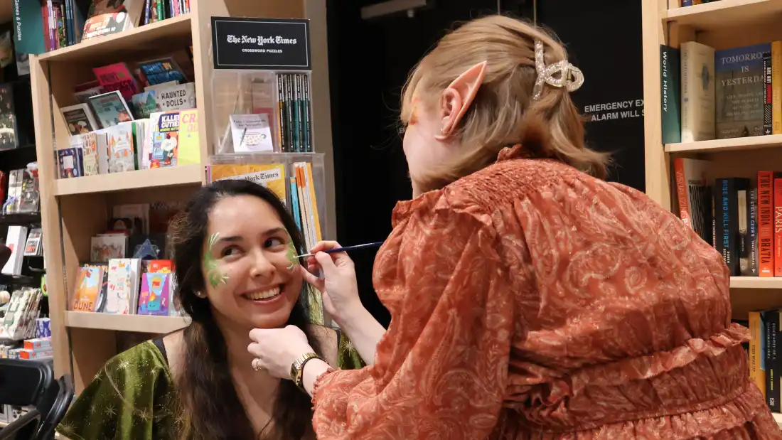 Dalia Luque, left, has her face painted by Amber Lovold, one of the organizers of a midnight release party at Politics and Prose in Washington, D.C. They are celebrating the publication of A Court of Splintered Harmony, the latest installment of Sarah J. Maas’ popular romantasy series.