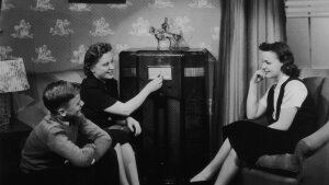 Two girls and a boy listen to a large valve radio in 1940.  