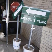 A sign that says "Measles Clinic" is shown. Two people are entering the Andrews County Health Department in Texas.