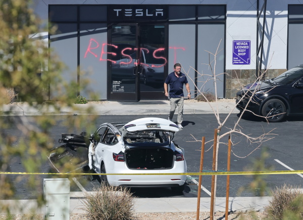 A man walks in a parking lot of a Tesla Collision Center in Las Vegas in front of a building with the word "RESIST" spray-painted on the door.