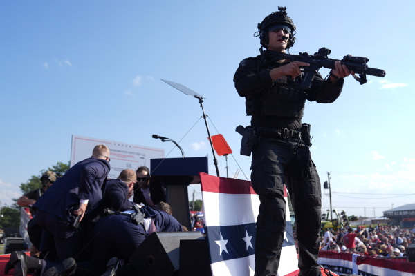 Republican presidential candidate Donald Trump is covered by U.S. Secret Service agents during the campaign rally in Butler, Pa., on July 13. The agents are wearing dark blue suits. In front of them is a law enforcement official prepared with a firearm.