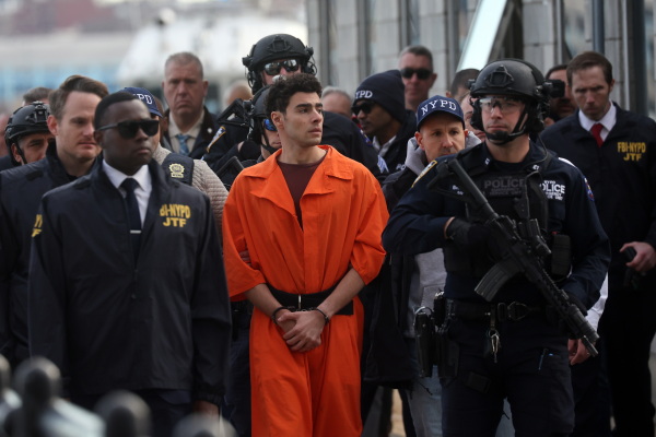 Luigi Mangione, wearing a bright orange jumpsuit, is surrounded by NYPD officers, including some with guns.