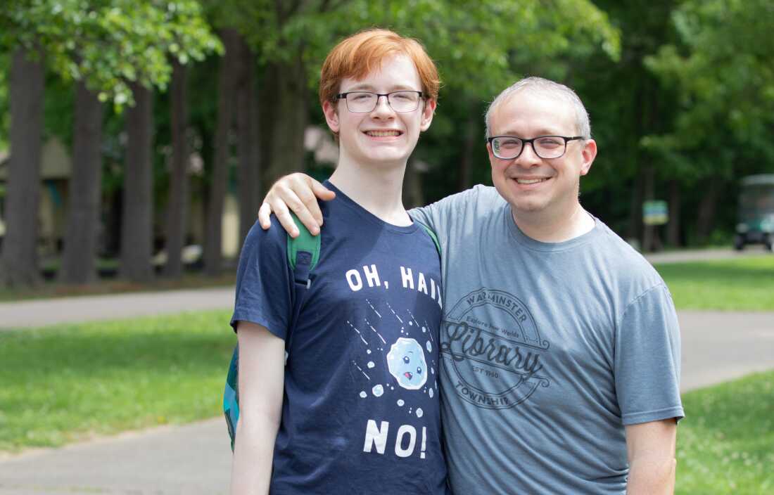 Tony Sadowski stands outdoors with his son, Bryan Sadowski, 18. The elder Sadowski has his arm around his son's shoulders, and both men are wearing T-shirts and glasses.