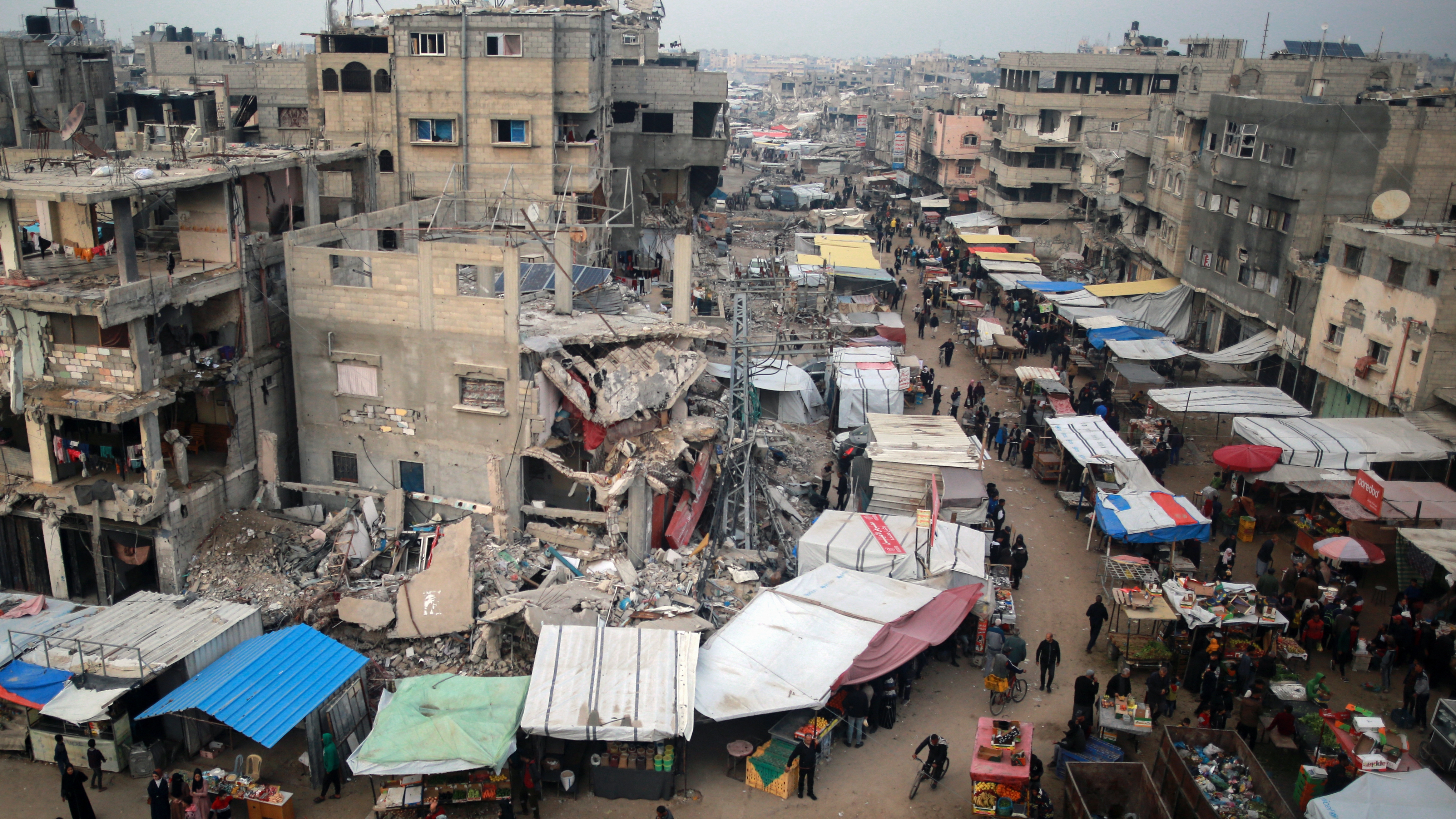 People walk past stalls selling goods amid the rubble of buildings destroyed during previous Israeli strikes, in Khan Yunis in the southern Gaza Strip on January 15, 2025.